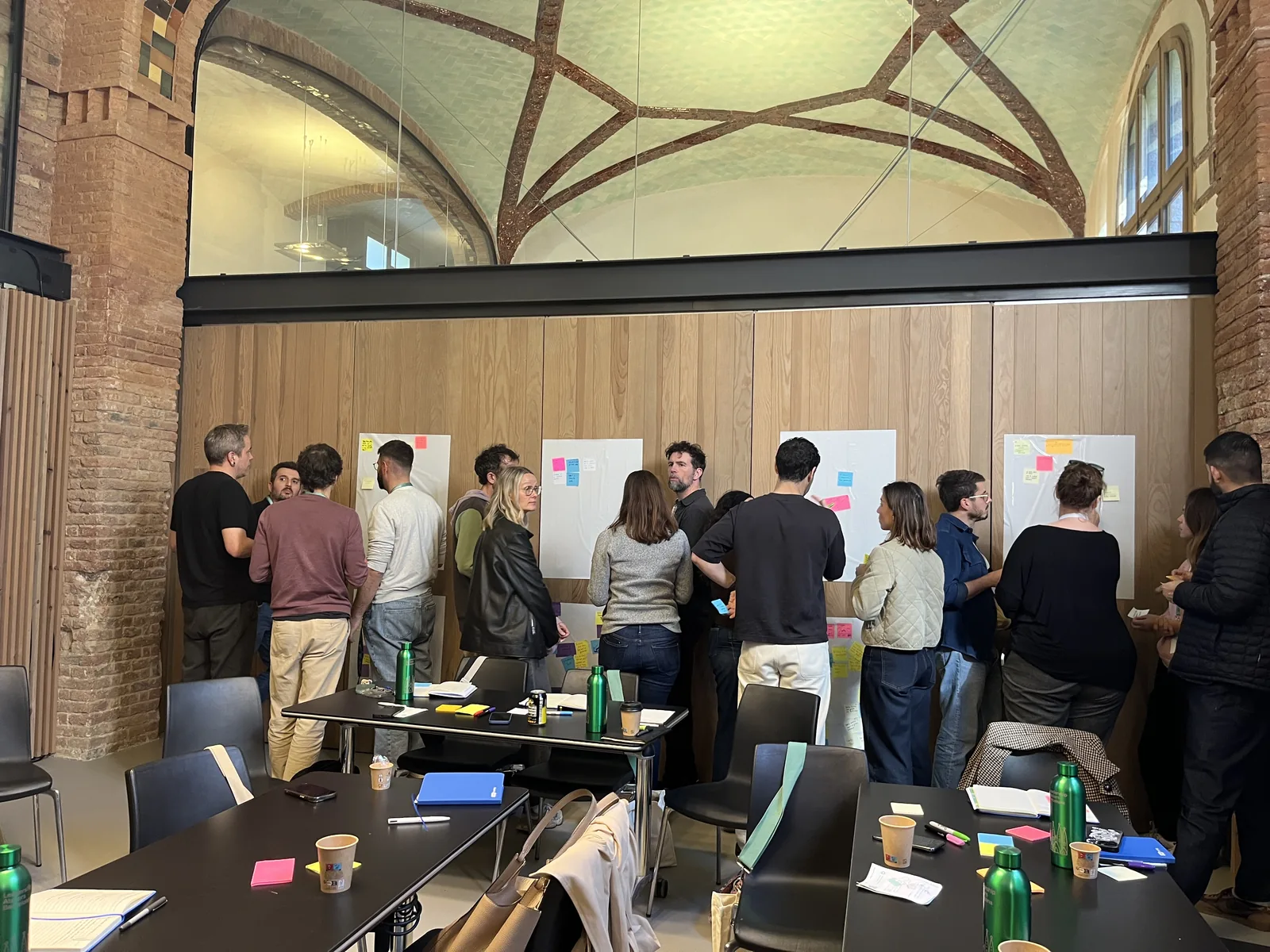 Workshop in progress: participants clustered at wall-mounted sheets, mapping and clustering with sticky notes